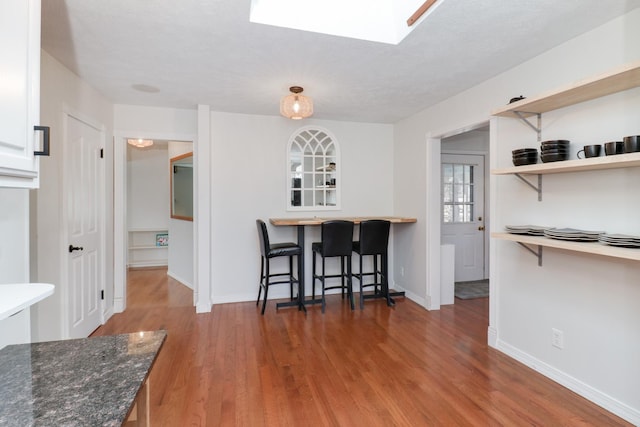 kitchen with dark stone countertops, a skylight, wood-type flooring, and a kitchen bar