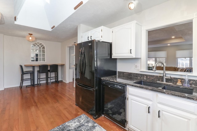 kitchen with sink, white cabinetry, dark stone countertops, black appliances, and a raised ceiling