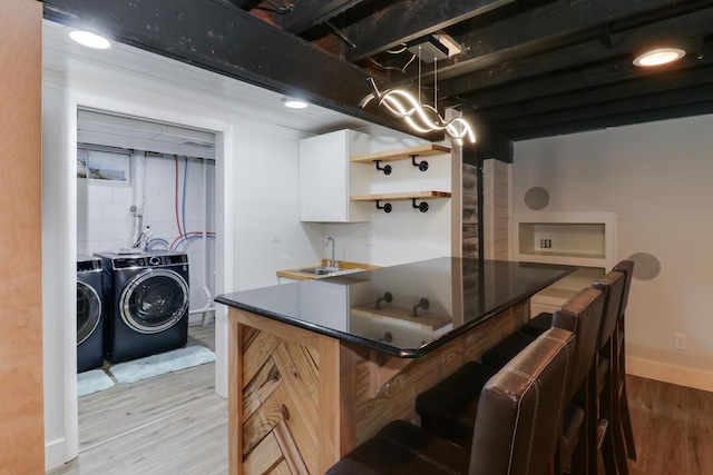 kitchen featuring a breakfast bar, white cabinetry, sink, washing machine and dryer, and light wood-type flooring