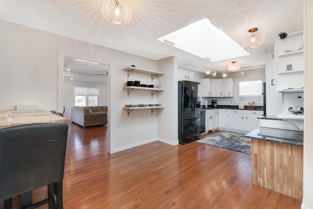 kitchen featuring white cabinetry, a skylight, a textured ceiling, dark hardwood / wood-style floors, and black appliances