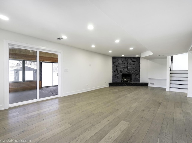 unfurnished living room featuring a stone fireplace and light wood-type flooring