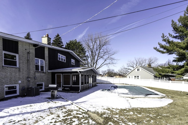 snow covered back of property featuring a sunroom, a covered pool, and central air condition unit