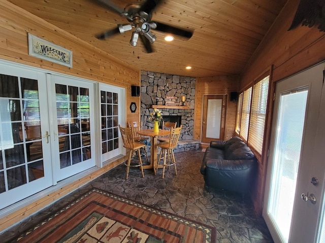 sunroom with lofted ceiling, wood ceiling, a stone fireplace, and ceiling fan