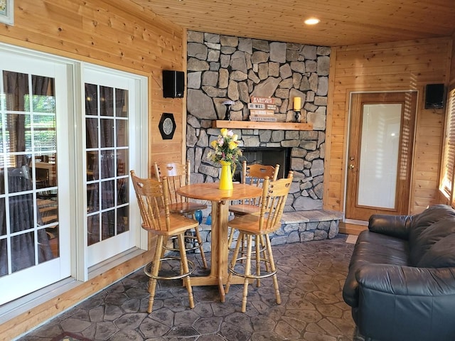 dining area featuring a fireplace, wood ceiling, and wooden walls