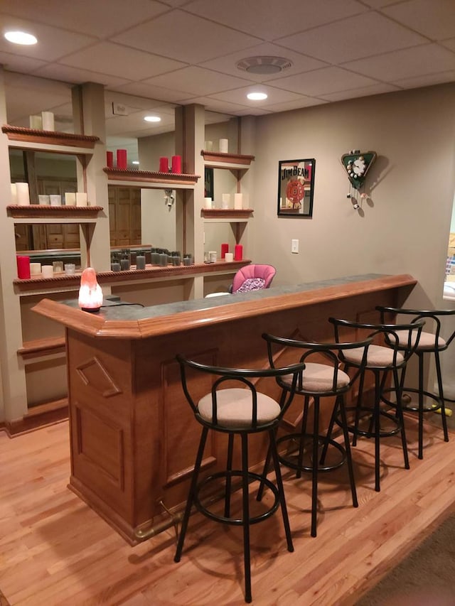 bar featuring a drop ceiling and light hardwood / wood-style flooring