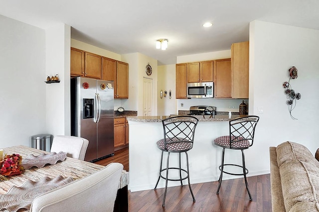 kitchen featuring dark wood-type flooring, a breakfast bar area, dark stone countertops, kitchen peninsula, and stainless steel appliances