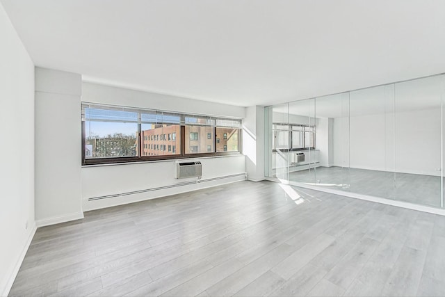 unfurnished living room featuring an AC wall unit, light wood-type flooring, and baseboard heating