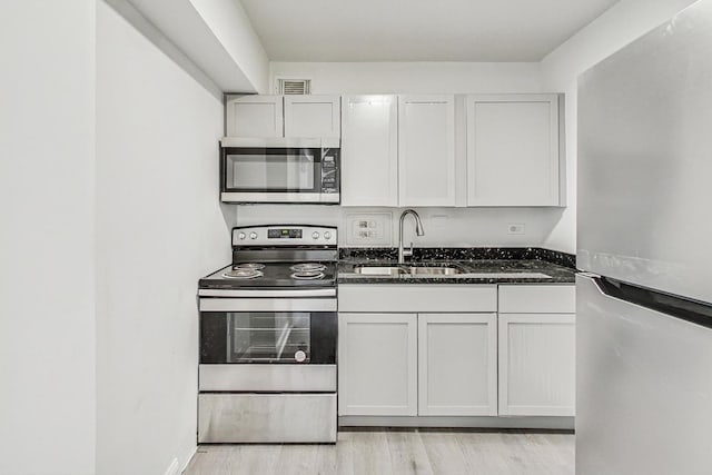 kitchen with white cabinetry, stainless steel appliances, sink, and dark stone counters