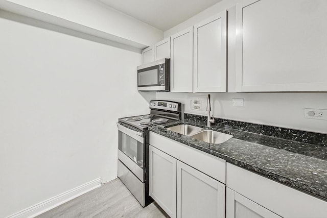 kitchen with sink, light hardwood / wood-style flooring, appliances with stainless steel finishes, dark stone countertops, and white cabinets