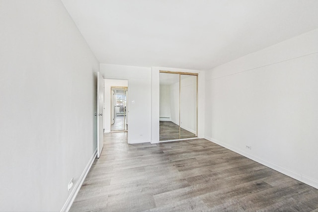 unfurnished room featuring hardwood / wood-style flooring and a baseboard heating unit