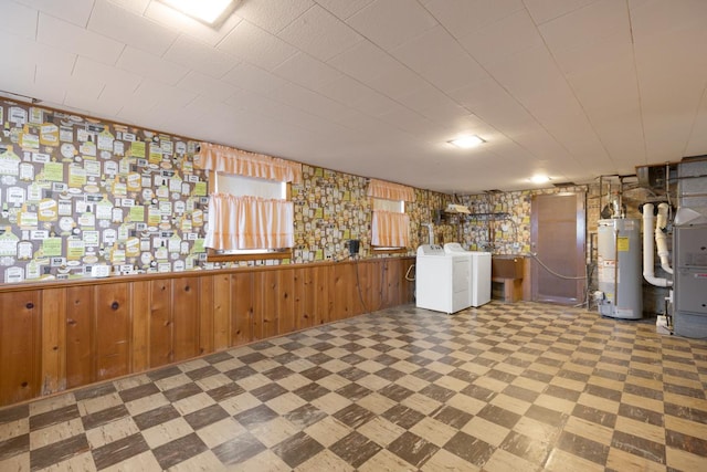 basement featuring sink, water heater, wooden walls, heating unit, and separate washer and dryer