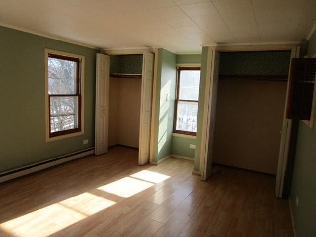 unfurnished bedroom with a baseboard heating unit, two closets, and wood-type flooring