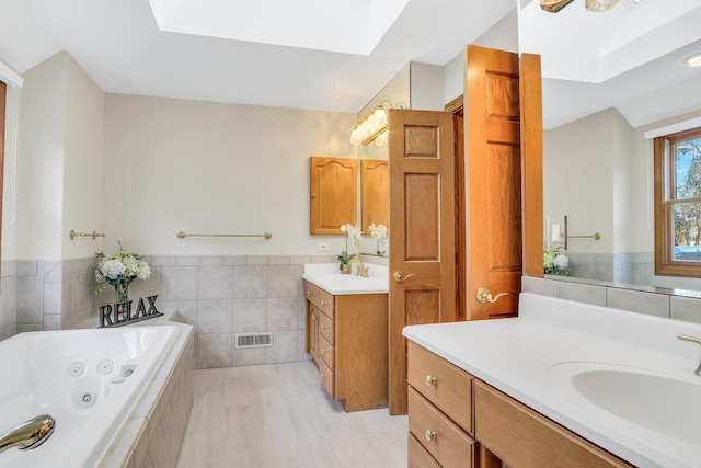 bathroom with vanity, tiled bath, tile walls, and a skylight