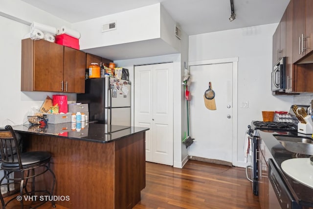 kitchen featuring dark wood-type flooring, a breakfast bar area, tasteful backsplash, kitchen peninsula, and stainless steel appliances