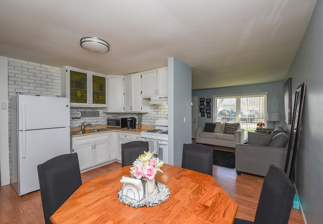 kitchen with tasteful backsplash, white cabinetry, sink, light wood-type flooring, and white appliances