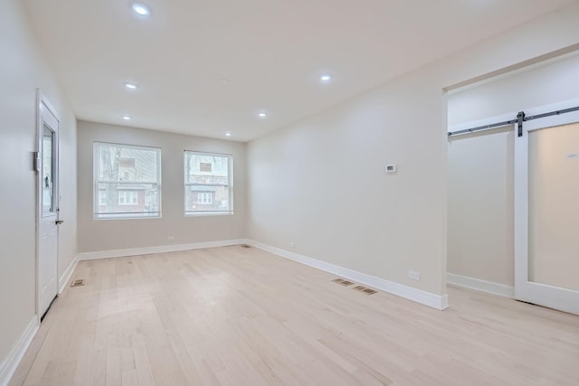 unfurnished bedroom featuring a barn door and light hardwood / wood-style flooring