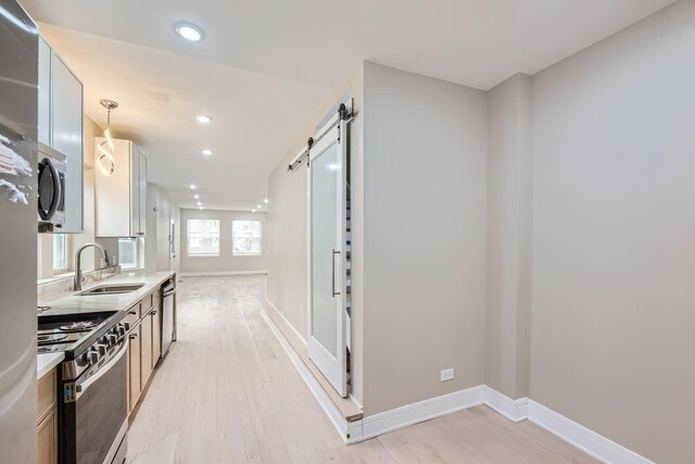 kitchen featuring pendant lighting, sink, stainless steel appliances, a barn door, and light hardwood / wood-style flooring