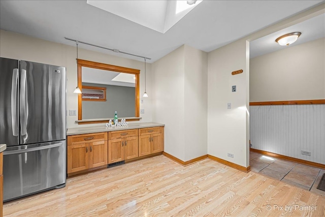 kitchen with light wood-style flooring, freestanding refrigerator, rail lighting, brown cabinetry, and light countertops