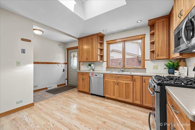 kitchen featuring open shelves, light wood-style flooring, appliances with stainless steel finishes, a skylight, and a sink