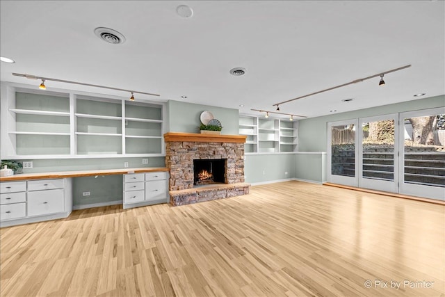 unfurnished living room featuring built in features, visible vents, light wood finished floors, a fireplace, and built in desk