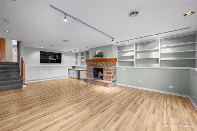 unfurnished living room featuring stairway, visible vents, a stone fireplace, rail lighting, and light wood-style floors