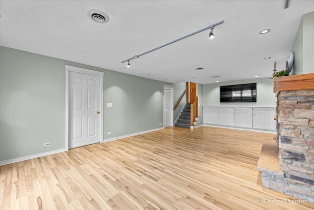 unfurnished living room featuring stairs, rail lighting, baseboards, and light wood-type flooring