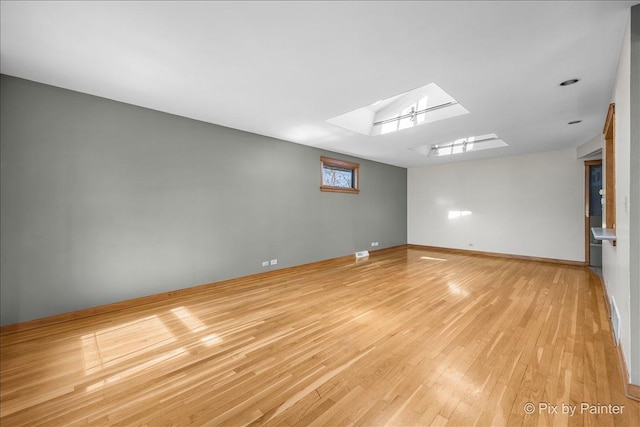 unfurnished room with visible vents, light wood-style flooring, a skylight, and baseboards