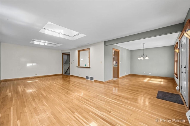 unfurnished living room with a notable chandelier, visible vents, a skylight, and light wood-type flooring