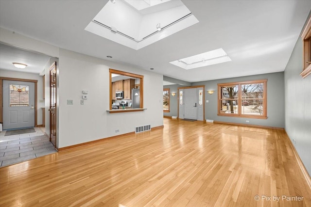 unfurnished living room with a skylight, light wood-style flooring, visible vents, and baseboards