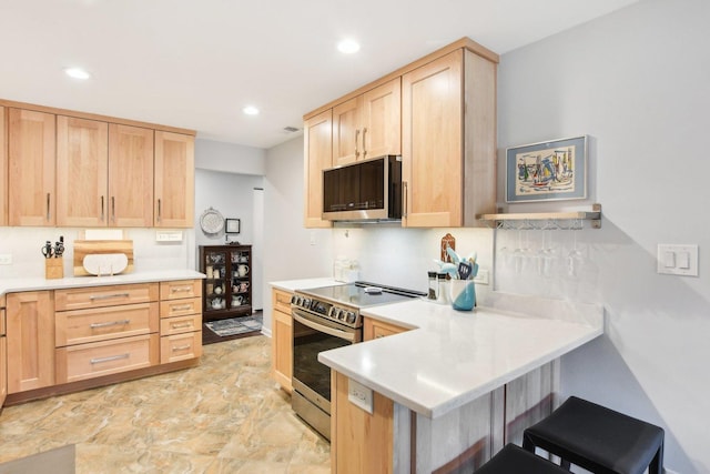 kitchen with light brown cabinetry, a kitchen breakfast bar, kitchen peninsula, and appliances with stainless steel finishes