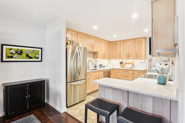 kitchen featuring appliances with stainless steel finishes, light brown cabinetry, sink, and kitchen peninsula