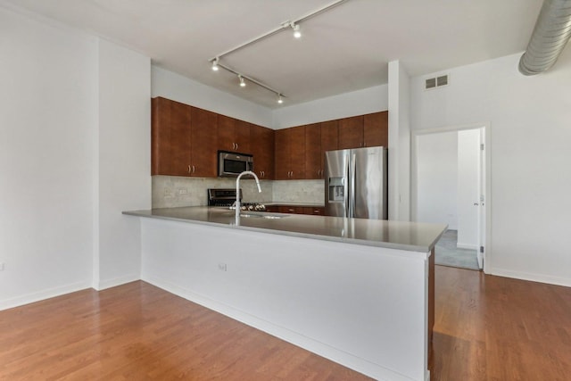 kitchen featuring sink, tasteful backsplash, kitchen peninsula, stainless steel appliances, and light hardwood / wood-style floors