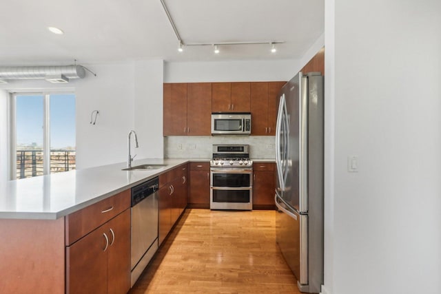 kitchen featuring appliances with stainless steel finishes, sink, backsplash, light hardwood / wood-style floors, and kitchen peninsula