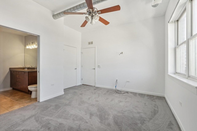 unfurnished bedroom featuring ceiling fan, ensuite bathroom, sink, and light colored carpet