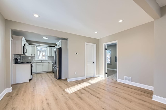 kitchen featuring appliances with stainless steel finishes, tasteful backsplash, white cabinetry, sink, and light hardwood / wood-style flooring