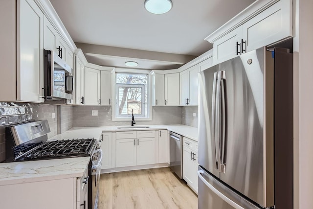 kitchen featuring sink, backsplash, stainless steel appliances, light stone counters, and white cabinets