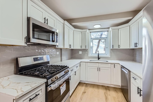 kitchen featuring sink, tasteful backsplash, light stone counters, stainless steel appliances, and white cabinets