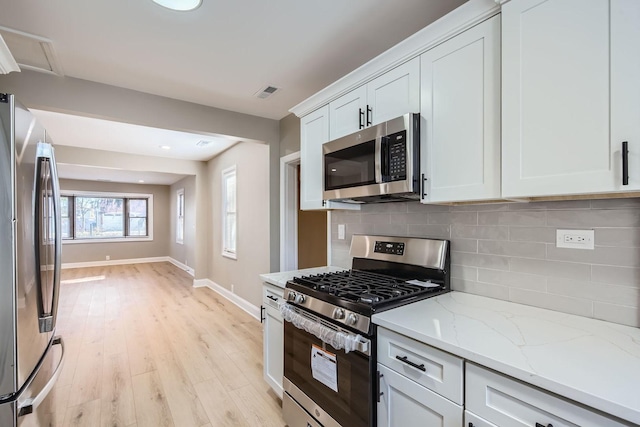 kitchen featuring white cabinetry, light hardwood / wood-style flooring, appliances with stainless steel finishes, light stone countertops, and decorative backsplash