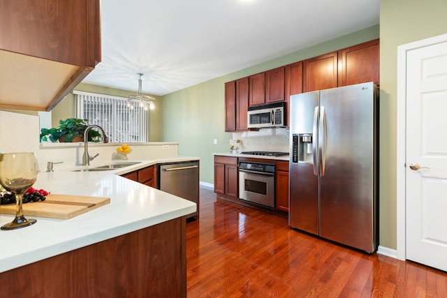 kitchen with sink, appliances with stainless steel finishes, kitchen peninsula, pendant lighting, and backsplash