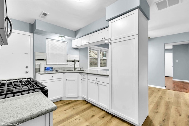 kitchen featuring sink, white cabinetry, decorative light fixtures, range with gas stovetop, and light hardwood / wood-style floors