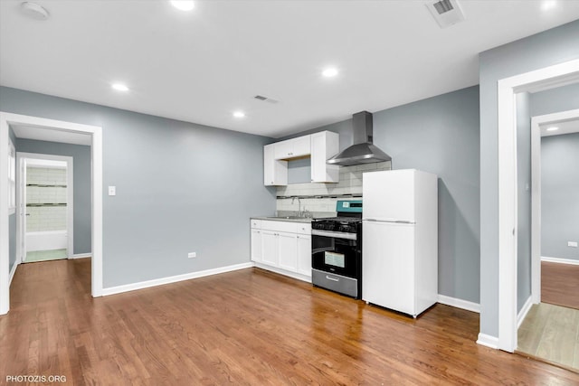 kitchen featuring gas range, white fridge, wall chimney range hood, hardwood / wood-style floors, and white cabinets