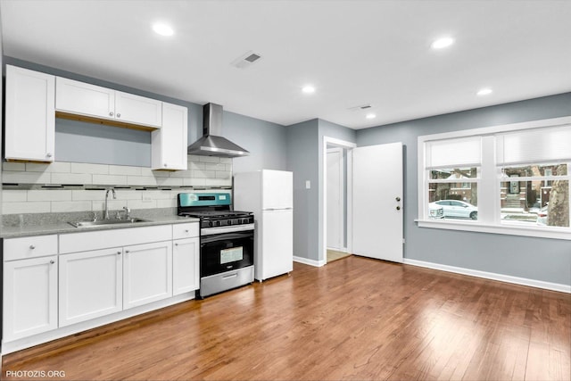 kitchen featuring wall chimney exhaust hood, sink, stainless steel gas stove, wood-type flooring, and white cabinets