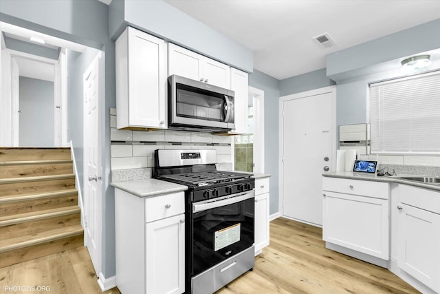 kitchen featuring backsplash, stainless steel appliances, white cabinets, and light wood-type flooring