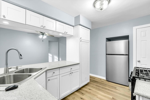 kitchen with sink, stainless steel refrigerator, white cabinetry, light hardwood / wood-style floors, and gas range