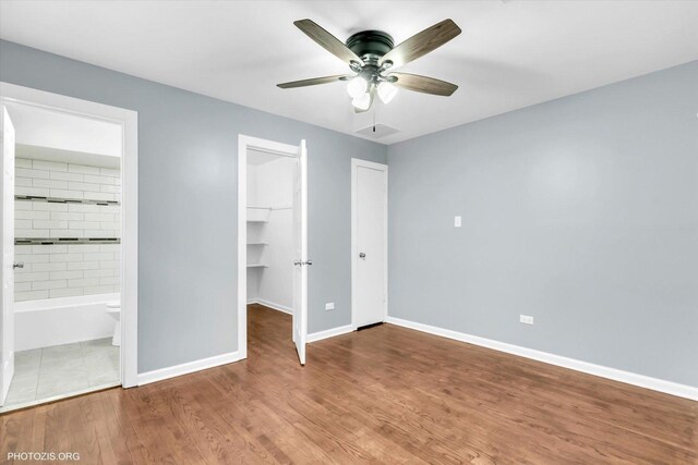 unfurnished bedroom featuring ensuite bath, a spacious closet, a closet, ceiling fan, and hardwood / wood-style floors