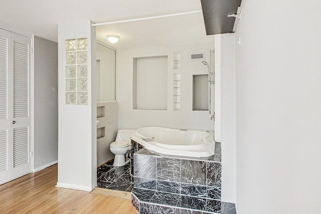 bathroom featuring a relaxing tiled tub, toilet, and hardwood / wood-style floors