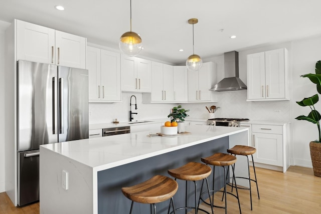 kitchen with hanging light fixtures, wall chimney exhaust hood, stainless steel appliances, sink, and white cabinetry