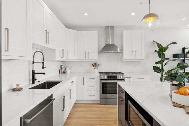 kitchen with appliances with stainless steel finishes, sink, white cabinetry, decorative light fixtures, and wall chimney exhaust hood