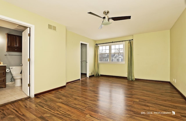 unfurnished bedroom with connected bathroom, a spacious closet, ceiling fan, dark wood-type flooring, and a closet