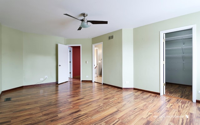 unfurnished bedroom with hardwood / wood-style floors, a spacious closet, a closet, and ceiling fan